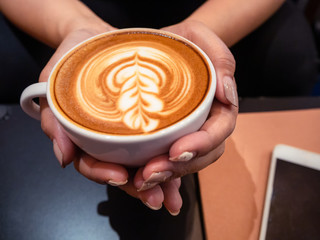 Hand woman holding a cup of hot latte arts coffee with cell phone and note on black table. Barista coffee art concept.with copy space