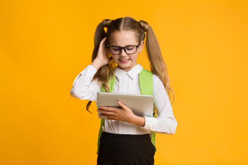Confused Schoolgirl Using Digital Tablet On Yellow Background