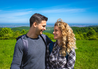 Young couple enjoying hiking together in nature standing on the top of the hill.