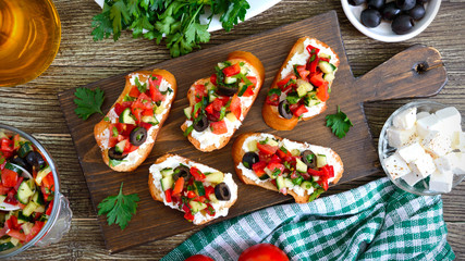 Delicious bruschettas with goat cheese and fresh vegetables. Crispy baguette slices with feta, tomatoes, cucumbers, peppers, olives, herbs. Healthy breakfast. Top view