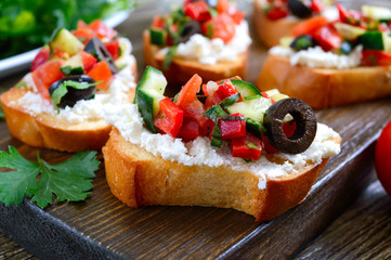 Delicious bruschettas with goat cheese and fresh vegetables. Crispy baguette slices with feta, tomatoes, cucumbers, peppers, olives, herbs. Healthy breakfast.