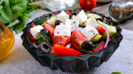 Tasty  vitamin salad with fresh vegetables, goat cheese, black olives, basil sauce on a white plate on a wooden background.