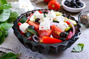 Tasty  vitamin salad with fresh vegetables, goat cheese, black olives, basil sauce on a white plate on a wooden background.