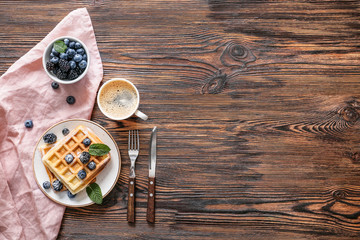 Tasty waffles with berries and cup of coffee on wooden table