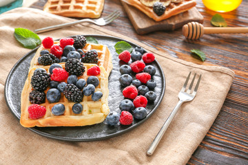 Plate with tasty waffles and berries on wooden table