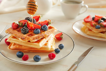 Pouring of honey onto tasty waffles with berries on plate