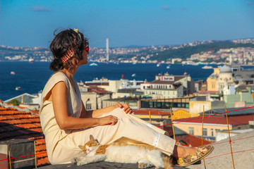 Fototapeta na wymiar Woman touching yellow cat at the roof with bosphorus background in Istanbul