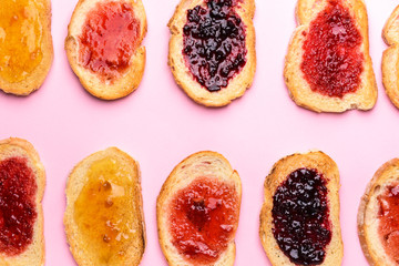 Tasty toasted bread with different jams on color background