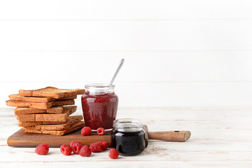 Board with tasty toasted bread and different jams on white table