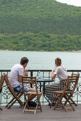 A guy and a girl are sitting at a table in an outdoor cafe near the lake waiting for the order.
