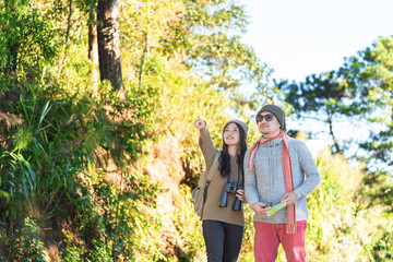 woman who is holding a binoculars points to something for the man who is her boyfriend while they are traveling into the wild in the morning on vacation