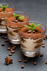 Classic tiramisu dessert in a glass cup on dark concrete background