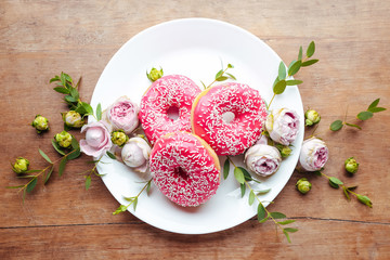 Plate with sweet tasty donuts and flowers on table