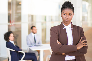 Stressed African American female employee standing with arms crossed and looking away. Her male and...