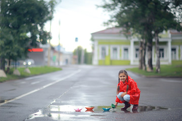 girl plays in paper boats in a puddle / autumn walk in the park, a child plays in the rain