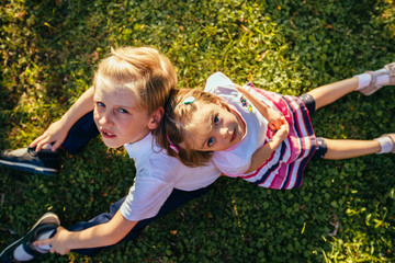 Top view two children sitting on the grass an summer time, looking in camera. Curiosity, pry, inquisitiveness childhood concept.