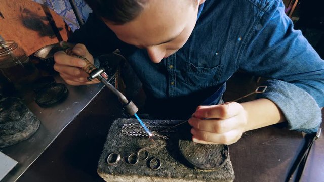 Jeweler makes a piece of jewelry. Male jeweler is heating a silver chain