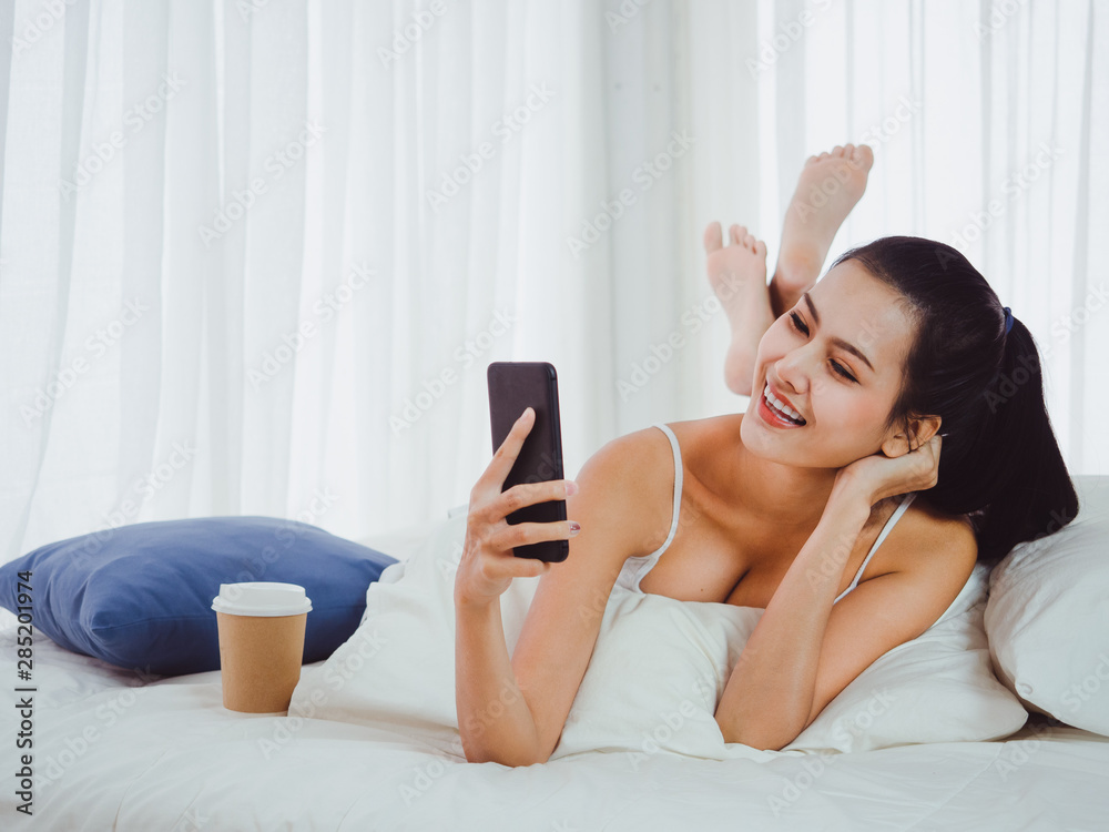 Wall mural Beautiful looking women are playing the phone on the bed,girl resting with coffee at home on holiday