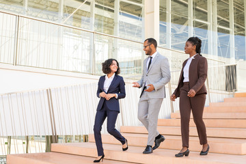 Cheerful business colleagues walking in office building. Three business man and women going down stairs, talking, laughing. Walking team concept