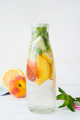 Homemade detox drink of lemon and peach in a bottle. Homemade lemonade on a white wooden table. Vertical orientation.