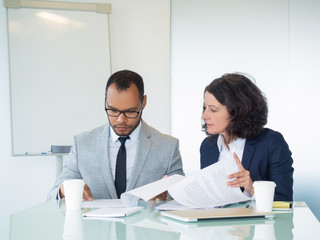 Office employees checking reports. Focused business man and woman sitting at meeting table and reading documents together. Paperwork and teamwork concept