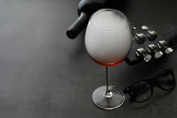 Guitar and high glass with red wine on a stone background.