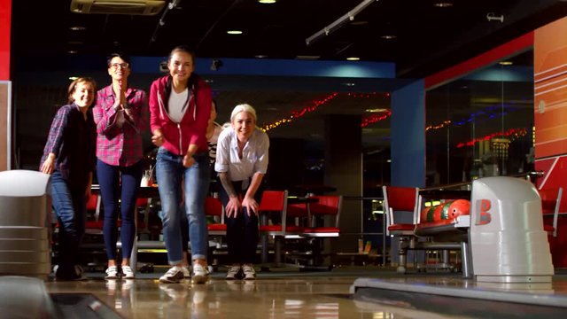 Medium shot with low angle of happy mature woman throwing bowling ball and celebrating knocking over pins with female friends. They are laughing and hugging