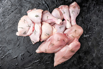 Raw chicken meat of fillets, legs and thighs on black background.