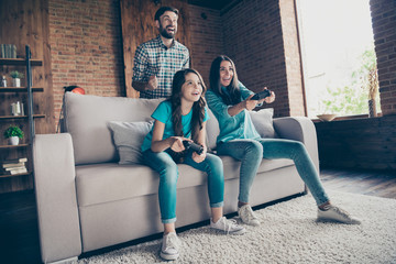 Portrait of excited people and little girl with brunet hair play videogame wearing denim jeans...