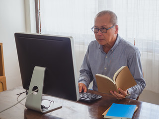 elder man read book and play computer in room