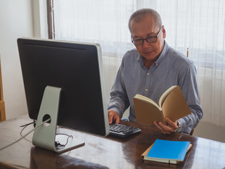 elder man read book and play computer in room