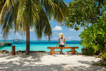 Fashion woman siting on a bench at the beach. Happy island lifestyle. White sand, blue cloudy sky...