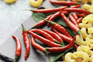 Uncooked pasta on a stone background. With seasonings and spices, spicy chili peppers.