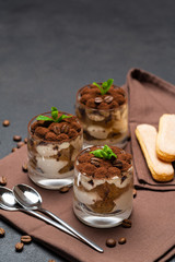 Classic tiramisu dessert in a glass cup on brown kitchen towel or napkin on dark concrete background