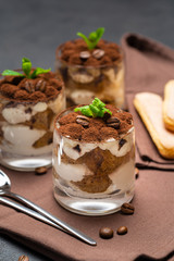Classic tiramisu dessert in a glass cup on brown kitchen towel or napkin on dark concrete background