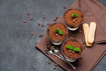 Classic tiramisu dessert in a glass cup on brown kitchen towel or napkin on dark concrete background