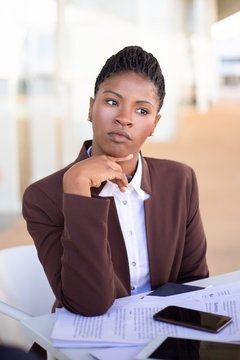 Pensive Young Businesswoman Thinking Over Contract Terms. Serious African American Business Woman Sitting At Table With Documents. Paperwork Concept