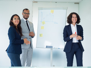 Team of interns and trainer posing near whiteboard with diagram. Three businesspeople standing in...