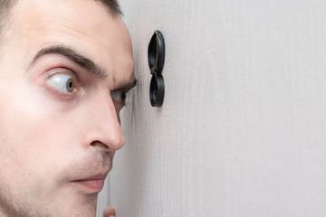 Man look out through the peephole of front door, portrait, closeup, toned