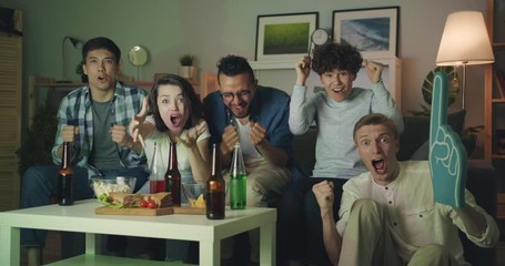 Slow motion portrait of excited students attractive young people watching sports game on TV at night cheering then doing high-five. Apartment, youth and emotions concept.