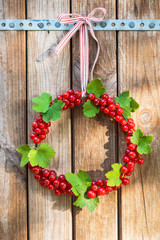 Summer wreath made of red currant berries and leaves tied with a bow hangs on old weathered wood. Garden decorations. Selective focus.