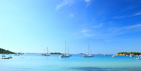 Beautiful blue sea in Camp Kosirina on Island Murter in Croatia, sailing ships in background