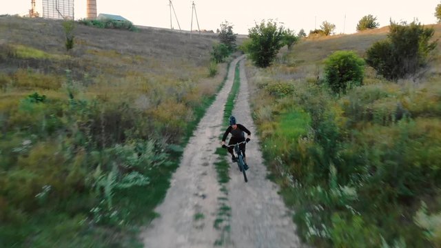 Aerial view cyclist racing along dirt road at sunset