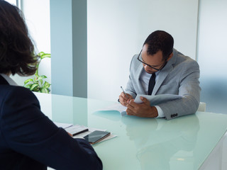 Businessman signing agreement at meeting. Business professional writing in document, while his...