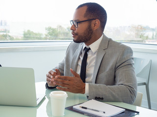 Serious young employee asking questions or explaining project details during meeting. Business man...