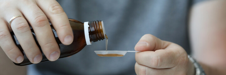 Male hand of man in hospital pours cough syrup from brown bottle into plastic spoon