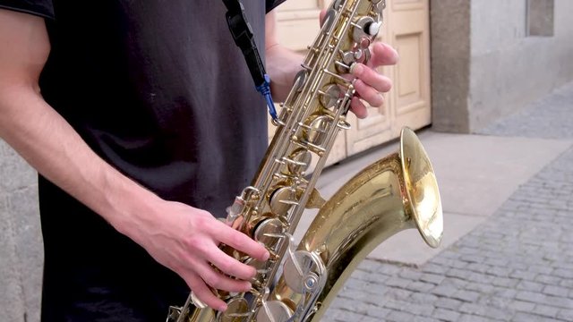 Unrecognisable white saxophonist in black play on golden saxophone. Live performance on street. Hands closeup. Jazz music