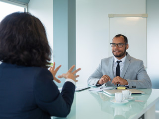 Obraz premium Excited male employer interviewing female applicant. Business man and woman sitting at conference table opposite of each other and talking. Career concept