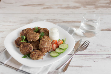 Juicy delicious meat cutlets in a white plate on a light wooden table.