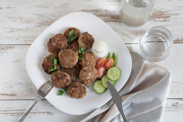 Juicy delicious meat cutlets in a white plate on a light wooden table.